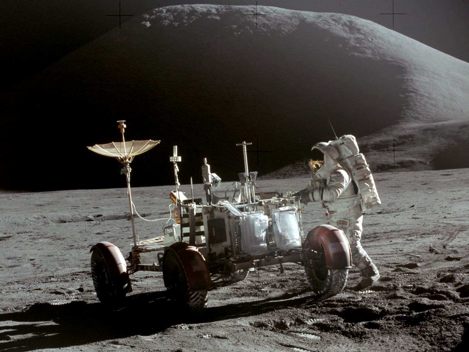 An Apollo 15 astronaut beside the Lunar Roving Vehicle on the Moon, a dark mountain behind.